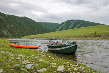 A fishing raft and kayak anchor on grass bank beside the river