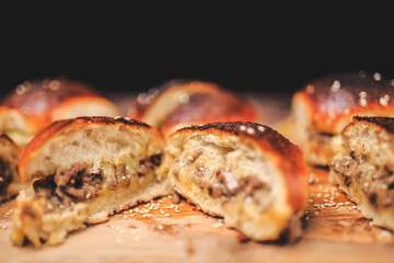 Homemade beef burger with cheese sliced in half with other burgers on the side on a wooden board with free space for text/decoration. Interior view of the burger.