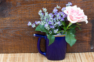 On a wooden background is a bouquet of lavender flowers and a pink rose.