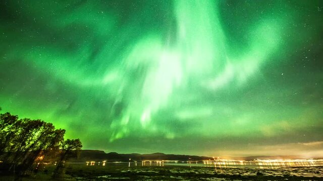 A magnificent light show on the night sky. Northern lights above Alta, Norway. Aurora dancing in the sky, changing shapes and shades. The yellow lights of the city are twinkling in the distance