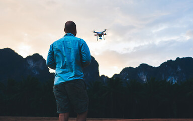 Back view of man wanderer is shooting video with radio controlled drone, agaist silhouette of rock...