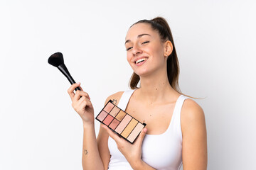 Young brunette woman over isolated white background with makeup palette and happy