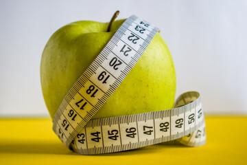 Green apple with tape measure on white and yellow background