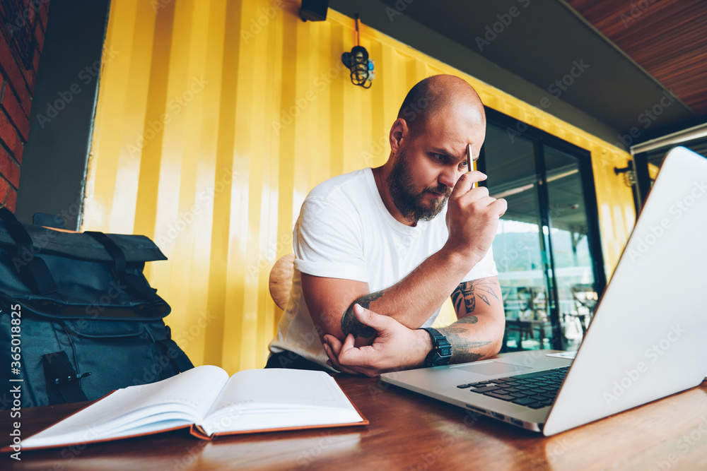 Poster concentrated male student puzzled on solving problem watching online tutorial during courses via lap