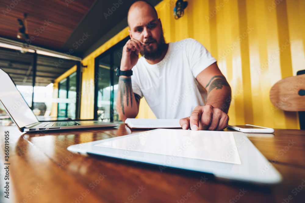 Poster serious hipster guy puzzled on idea for new online project pressing button on portable pc for networ