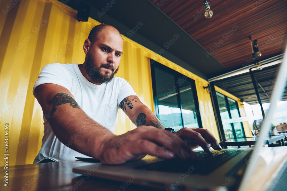 Poster worried caucasian hipster guy concentrated on playing video game on laptop computer, serious millenn