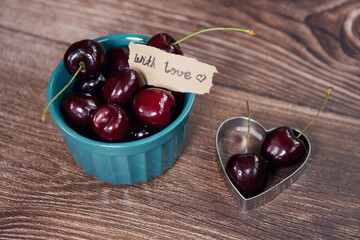 Ripe berries of cherries in bowl and in cookie cutter heart shape with text With Love on wooden...