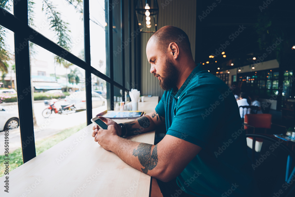Poster young hipster guy checking new updates of social networks content via smartphone on break in cafeter