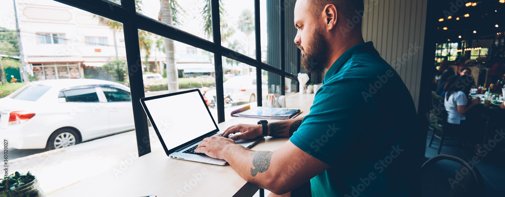 Poster serious bearded male blogger typing message on laptop computer with mock up screen chatting in socia