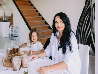 Obraz premium mother and daughter sitting at the table and having breakfast. Food, family, morning, rituals concept