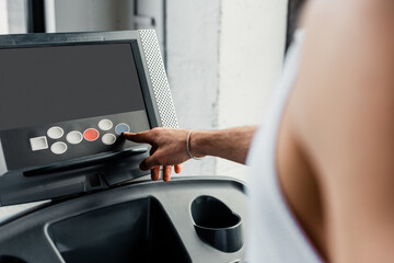 cropped view of sportsman pointing with finger at button on treadmill in gym