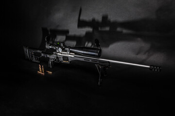 Modern black sniper rifle with optical sight on a dark back. Bolt carbine stands on sockets....