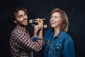 Young couple in love eat sushi on bruderschaft, enjoys and having fun together. Studio photo