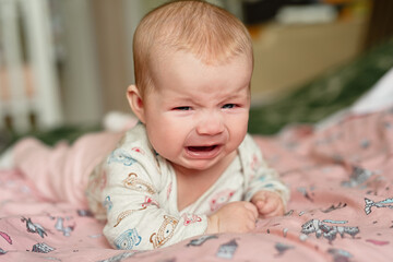 three month old girl crying, lies on his stomach and is very upset, sad emotions in  child