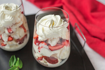Eton Mess - summer healthy dessert with whipped cream, meringue, strawberry in glasses on a table.