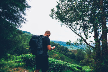 Young man tourist with travel backpack walking in mountains and searching right direction on navigator on modern smartpone.Male hiker with rucksack holding telephone while exloring natural environment