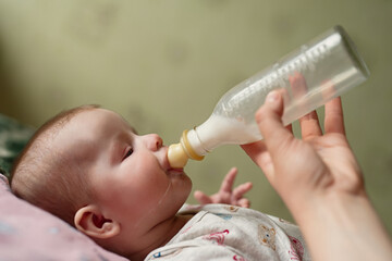 newborn baby eats milk from bottle, drops of food run down  cheek, dad gives baby  mixture