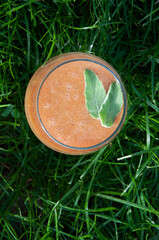 Koktajl owocowy z listkami miety w szklanym naczyniu, w tle trawa.
