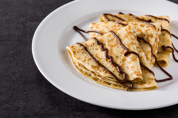 Sweet crepes with chocolate on black background
