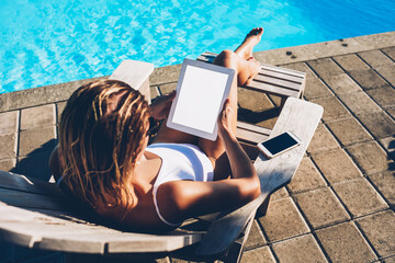 Top view of young woman resting on sunbed and working remotely in same time using internet and digital tablet with blank copy space screen for information content enjoying to earn money in summertime