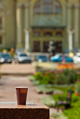 Brown paper cup on a background of urban architecture. Coffee on a marble border. The houses of the old town are blurred in the background. Sharpness on coffee. Layout for design.