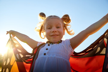 Young and small cute girl with bright fabric like butterfly wings play, fly, run, jump in meadow or...