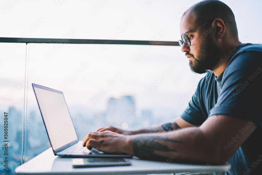 Poster cropped image of handsome confident freelancer in trendy eyewear typing message to customer via appl