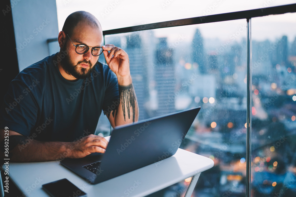Poster young handsome skilled it developer correcting trendy eyeglasses while watching training webinar in 