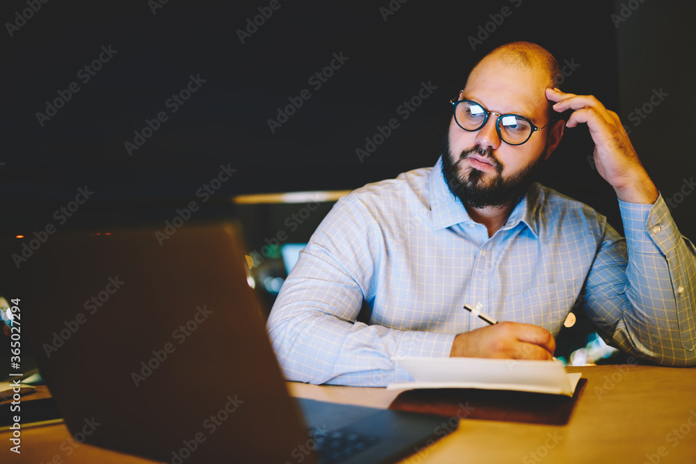 Poster pensive male blogger writing in notepad review watching online movie on laptop computer at home inte