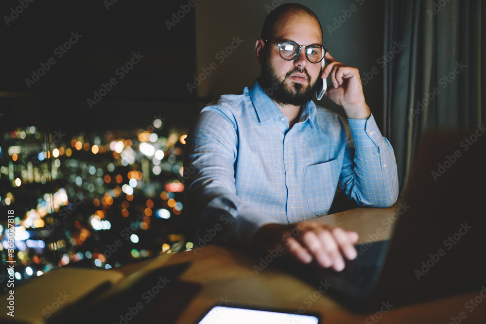 Poster serious male freelancer talking with customer support operator on telephone installing application o