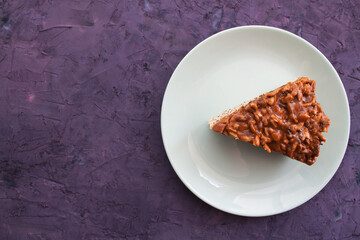 piece of pie covered with caramel and sunflower seeds in light blue plate on a right sight of a violet grunge background
