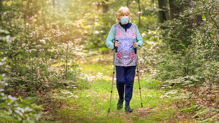 Senior woman hiking on a wooded path with COVID-19 face protection
