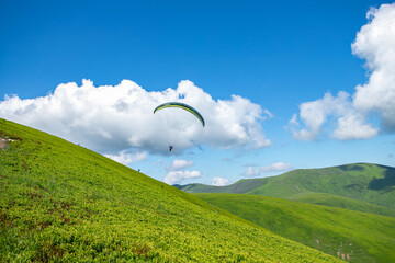 Paragliding in the Carpathians in the summer.Two paragliders fly over a mountain valley on a sunny summer day. Beautiful landscape with greenery and people paragliding. Rest and travel.