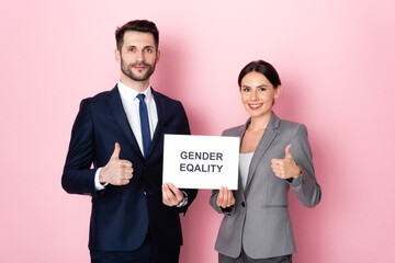 handsome businessman and businesswoman holding placard with gender equality lettering and showing thumbs up on pink
