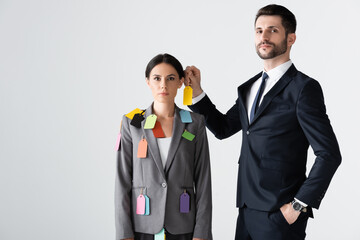 bearded businessman standing with hand in pocket and putting label on beautiful businesswoman...