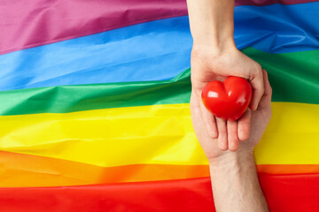 Male hands hold heart on LGBT flag, top view