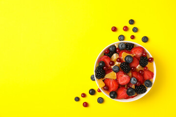 Bowl of fresh fruit salad on yellow background, top view