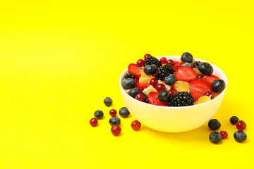 Bowl of fresh fruit salad on yellow background, space for text
