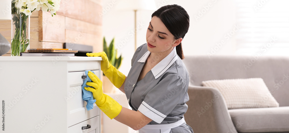 Wall mural young chambermaid wiping dust from furniture in hotel room. banner design