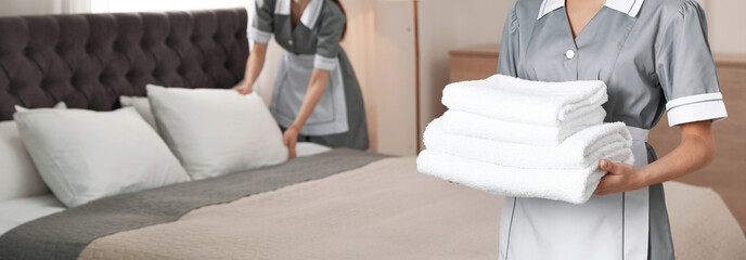 Chambermaid holding stack of fresh towels in hotel room, closeup view with space for text. Banner...