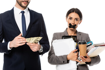 bearded businessman holding dollars near businesswoman with duct tape on mouth isolated on white,...