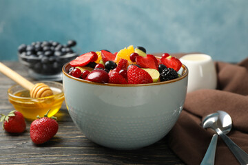 Composition with bowl of fresh fruit salad on wooden background, close up