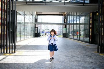 happy girl schoolgirl 8 years of European appearance with a backpack sitting goes in school uniform in the school yard looking at the camera closeup