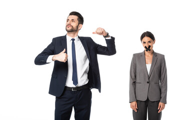 arrogant businessman in suit pointing with thumbs at himself near woman with scotch tape on mouth isolated on white