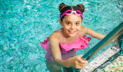 Happy beautiful little smiling girl in goggles and swimsuit in the pool has fun while vacationing...