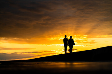 Silhouette of a couple enjoying beautiful golden sunset at the seaside  