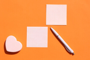 Colored sheets of paper for notes and a small heart on an orange background. Close-up. Top view, copy space