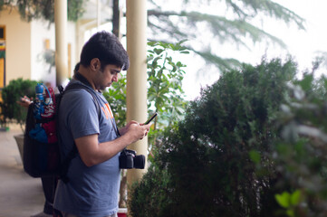 Young indian male in t-shirt messaging emailing connecting on mobile while on vacation with a beautiful foggy background and greenery