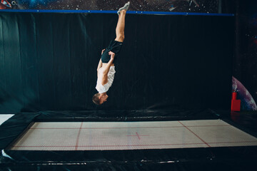Young man acrobat jumping on trampoline indoor