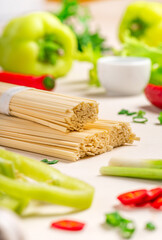 Uncooked dry udon noodles and raw vegetables on a white background, selective focus.